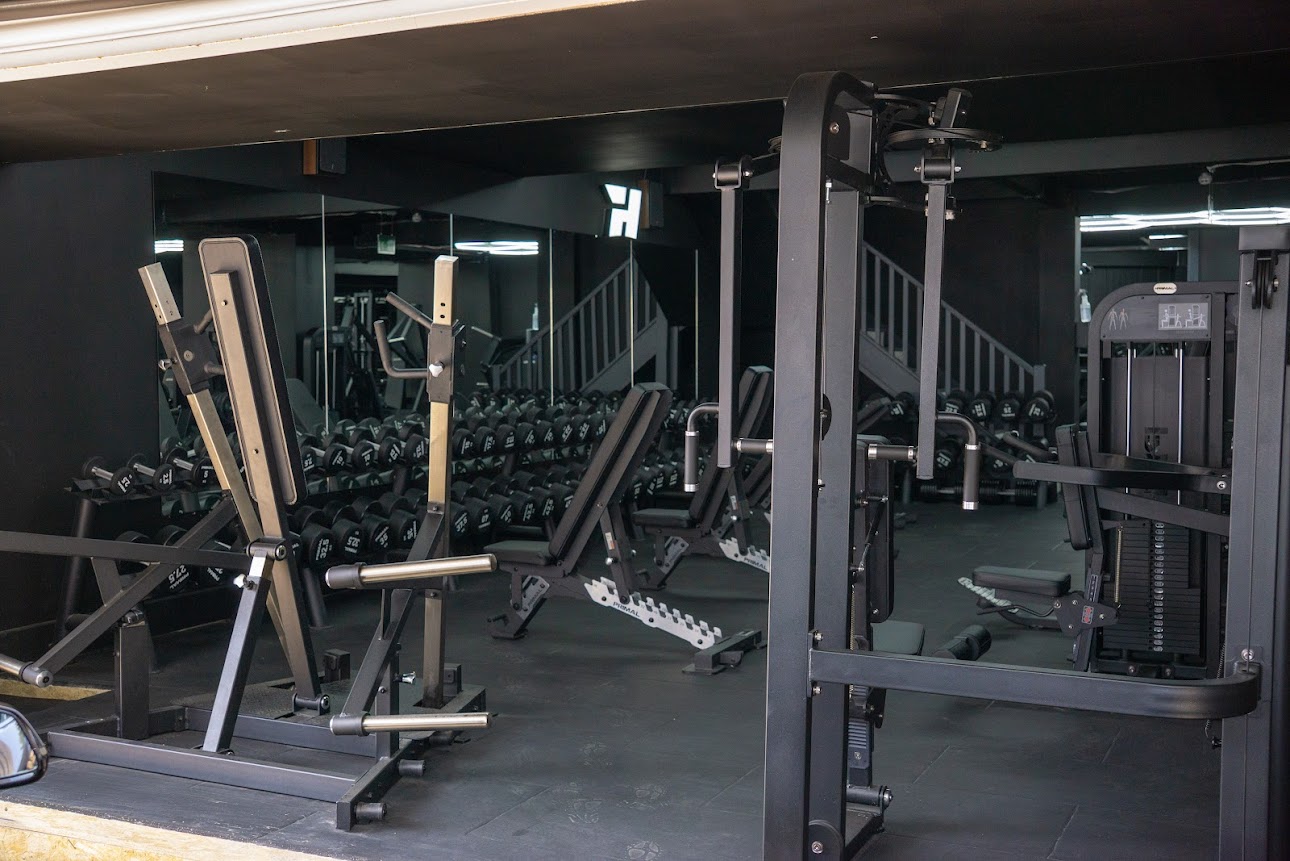 Gym floor with T-bar row, cable machines and mirror wall under stairs